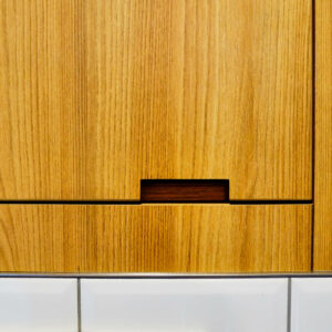 Détail de menuiserie sur mesure en stratifié avec poignée découpée et raccord inox-carrelage dans les sanitaires d’une entreprise à Liège