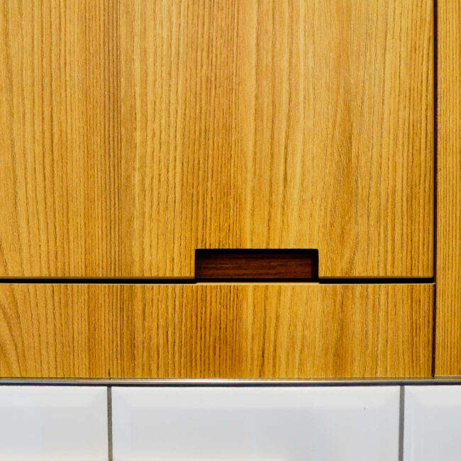 Détail de menuiserie sur mesure en stratifié avec poignée découpée et raccord inox-carrelage dans les sanitaires d’une entreprise à Liège