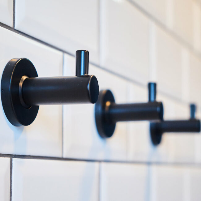 Porte-manteau mural noir sur carrelage métro blanc – détail de l’aménagement des sanitaires d’une entreprise à Liège