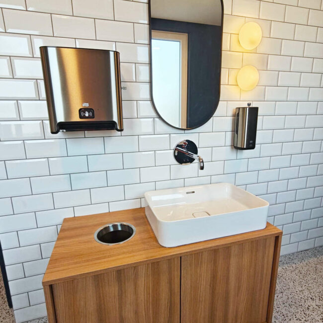 Aménagement de sanitaires d’entreprise à Liège avec meuble lavabo sur mesure, carrelage métro et miroir vertical