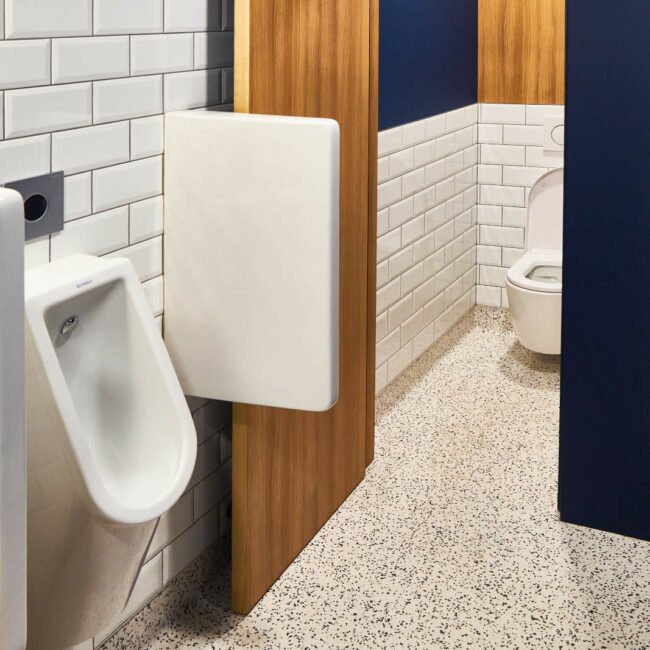 Aménagement des WC hommes dans les sanitaires d’une entreprise à Liège avec carrelage métro, sol en linoléum et cloisons en menuiserie sur mesure